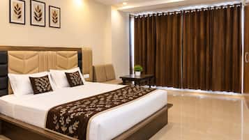 A hotel room with a large bed, a headboard, a bedside table with a plant, and a view of the outside through curtains.