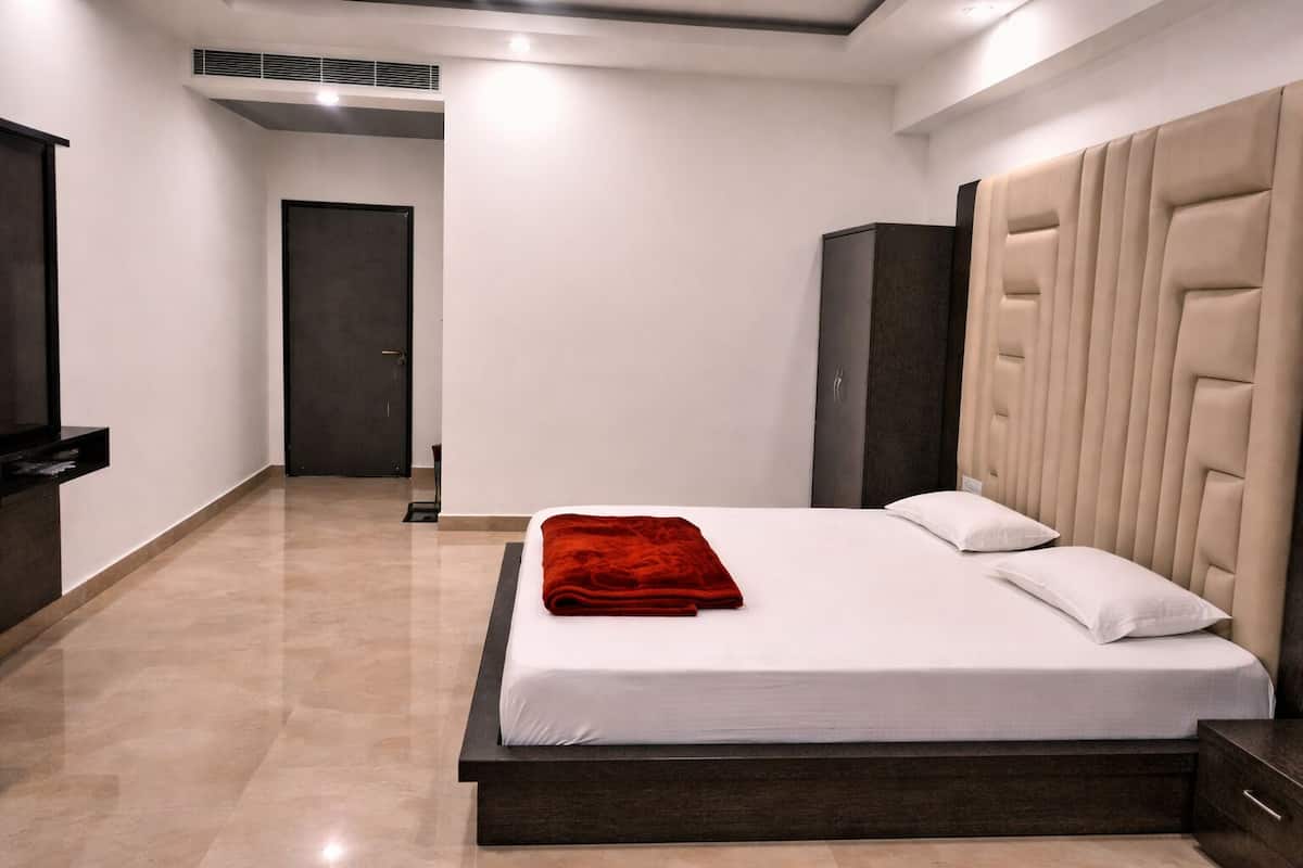A modern hotel room with a large bed, a dark headboard, and a flat-screen TV mounted on the wall.