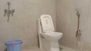 A bathroom with a toilet, a shower, and a blue bucket.