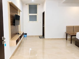 Una sala moderna con un televisor de pantalla plana montado en una pared de madera, un sofá beige, una mesa de centro de madera y una puerta que da a otra habitación.