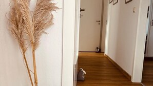 Um corredor com piso de madeira, um vaso de vidro com plumas de capim-do-campo e uma porta que dá para outro cômodo.