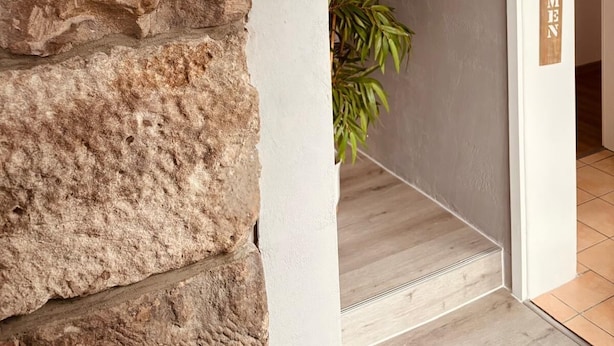 Um muro de pedra, um vaso com planta e um letreiro com a palavra 'WILKOMEN'.