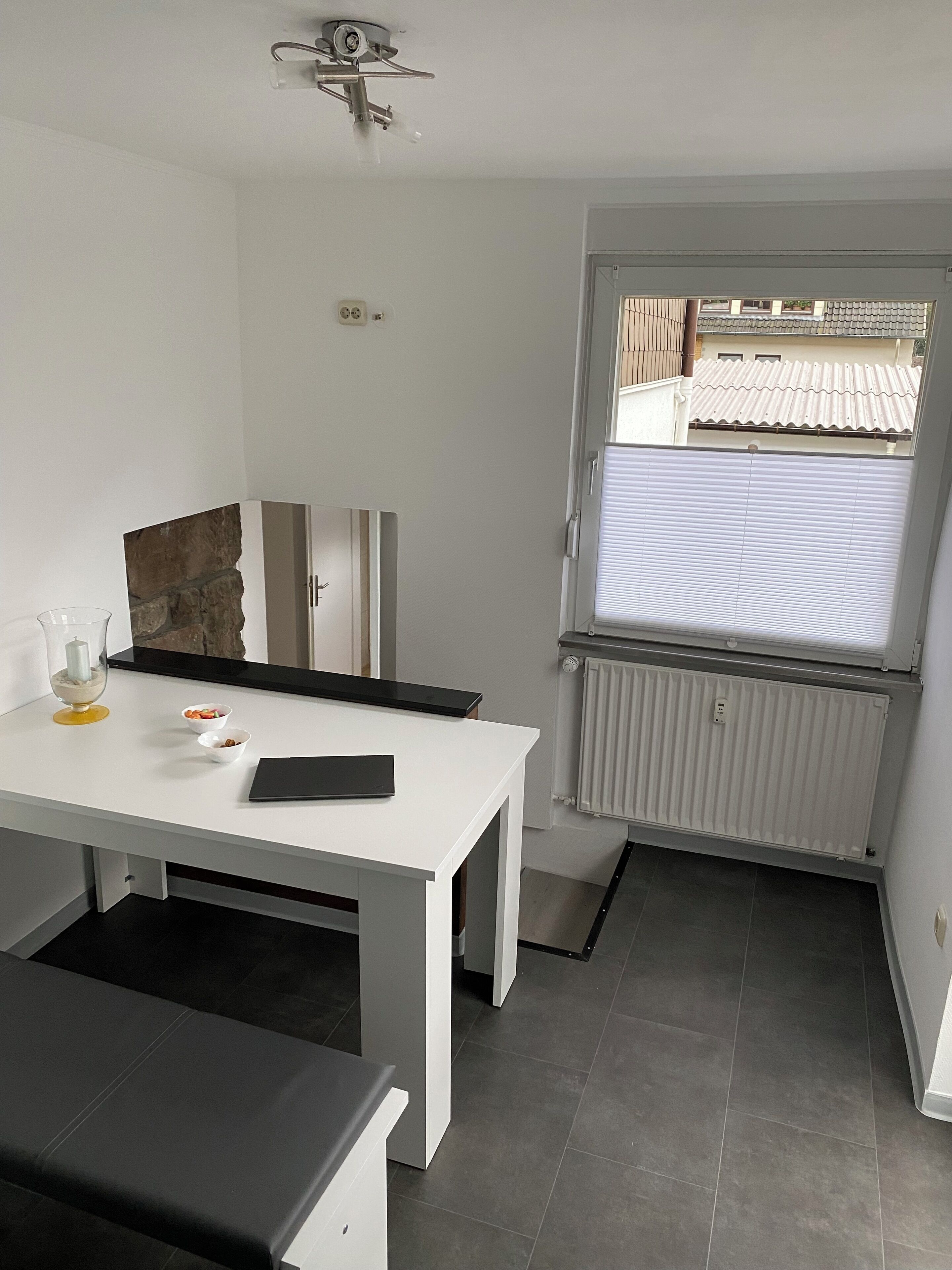 A small, modern kitchen with a white countertop, a black table, and a window with a view of a tiled roof.
