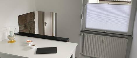A small, modern kitchen with a white countertop, a black table, and a window with a view of a tiled roof.