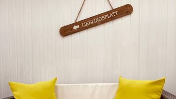 A wicker sofa with yellow cushions, a glass candle holder with a white candle, and a wooden sign above the sofa.