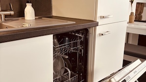 Uma cozinha moderna com máquina de lavar louça embutida nos armários, pia de aço inoxidável e dosador de sabão branco.