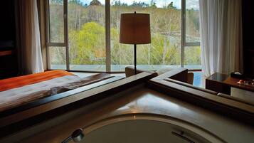 A hotel room with a bed, a bedside table, a lamp, and a view of a windmill and trees.
