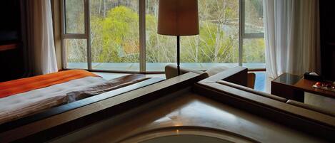 A hotel room with a bed, a bedside table, a lamp, and a view of a windmill and trees.
