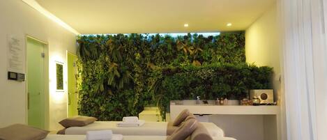 A modern hotel room with a green wall, two beds, a desk, and a bathroom.