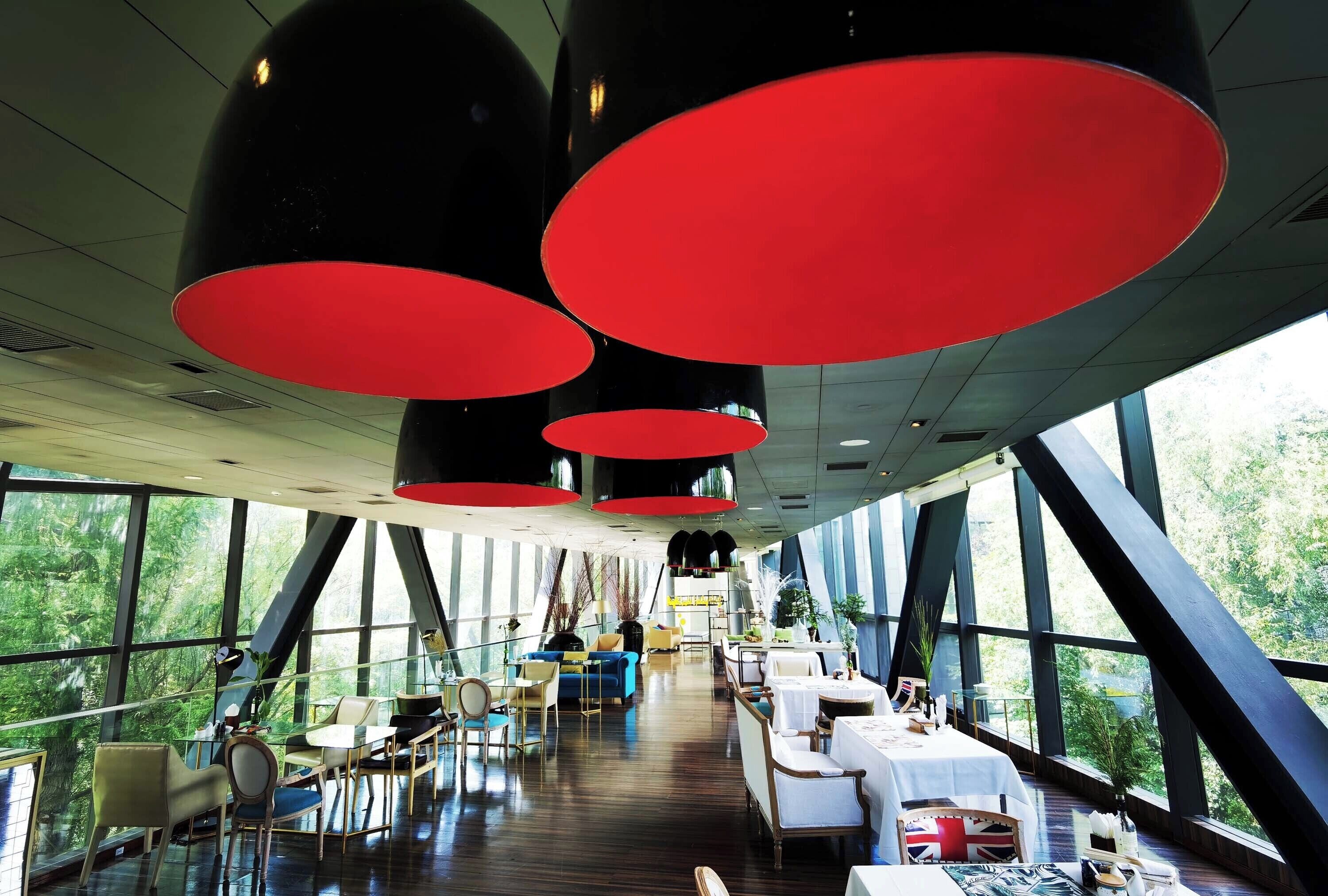 A modern dining area with large windows, red pendant lights, and a variety of seating arrangements.