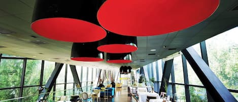 A modern dining area with large windows, red pendant lights, and a variety of seating arrangements.