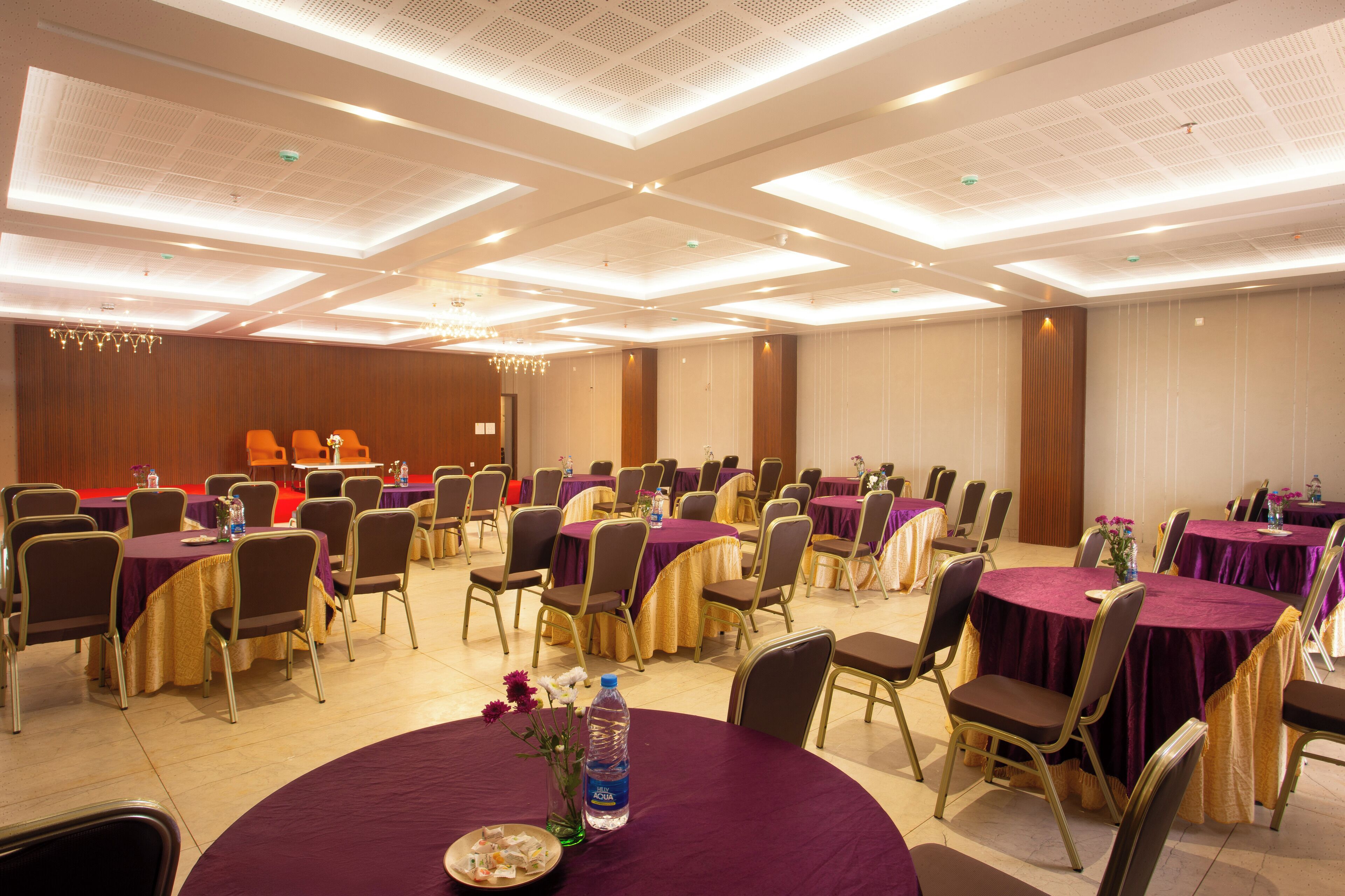 Una sala de banquets amb taules rodones cobertes amb mantells porpra, disposades per files amb cadires.