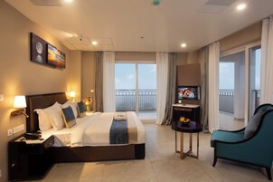 A hotel room with a large bed, a TV, a desk, and a balcony with a view.