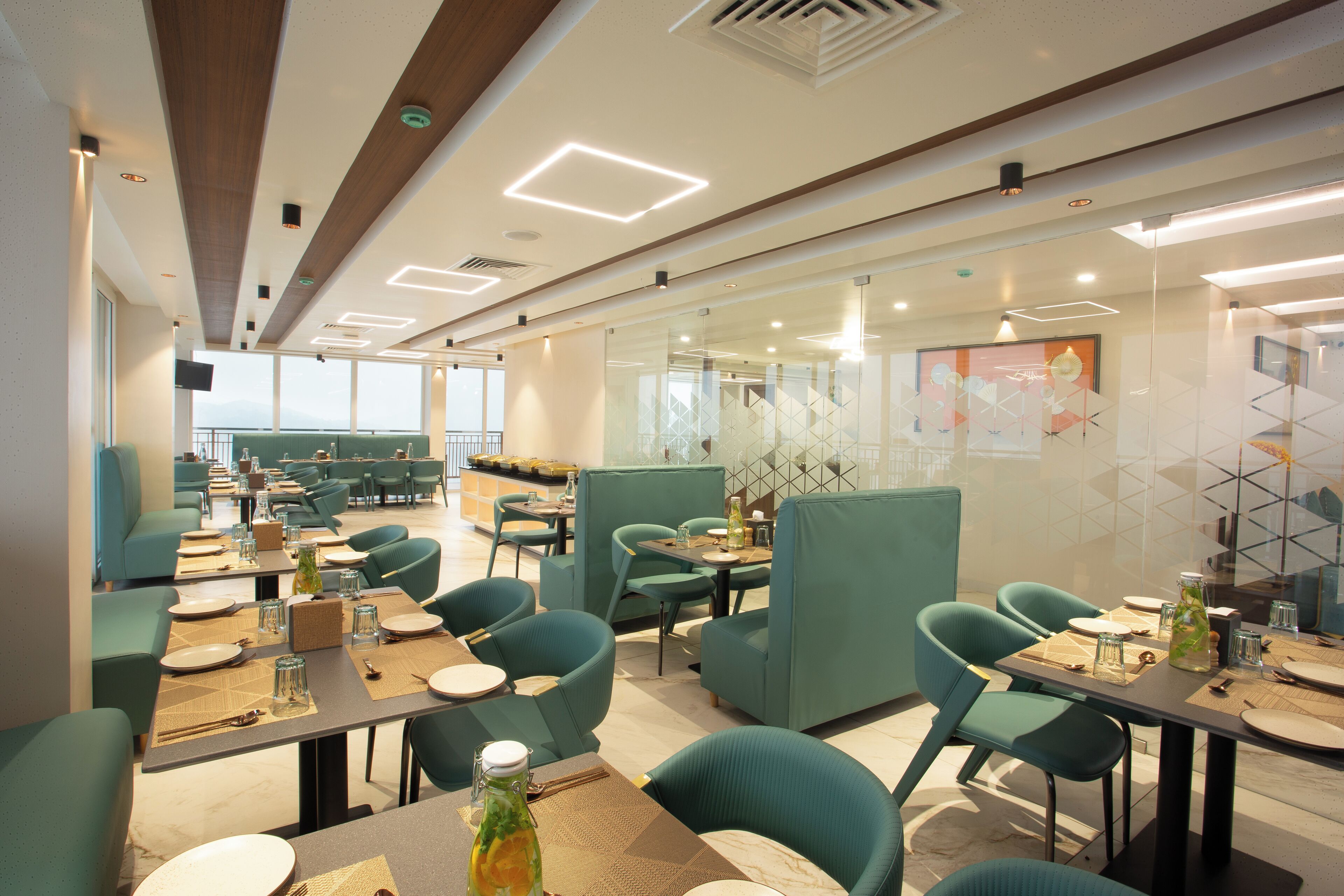 A modern restaurant with teal upholstered chairs and tables, geometric wall decor, and a view of the cityscape through large windows.