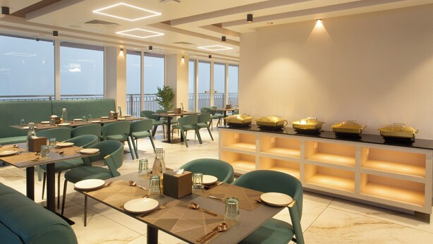 A modern restaurant with green seating, a buffet area, and large windows offering a view. - Le Crown Hotel (Vagamon)