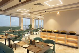 A modern restaurant with green seating, a buffet area, and large windows offering a view.