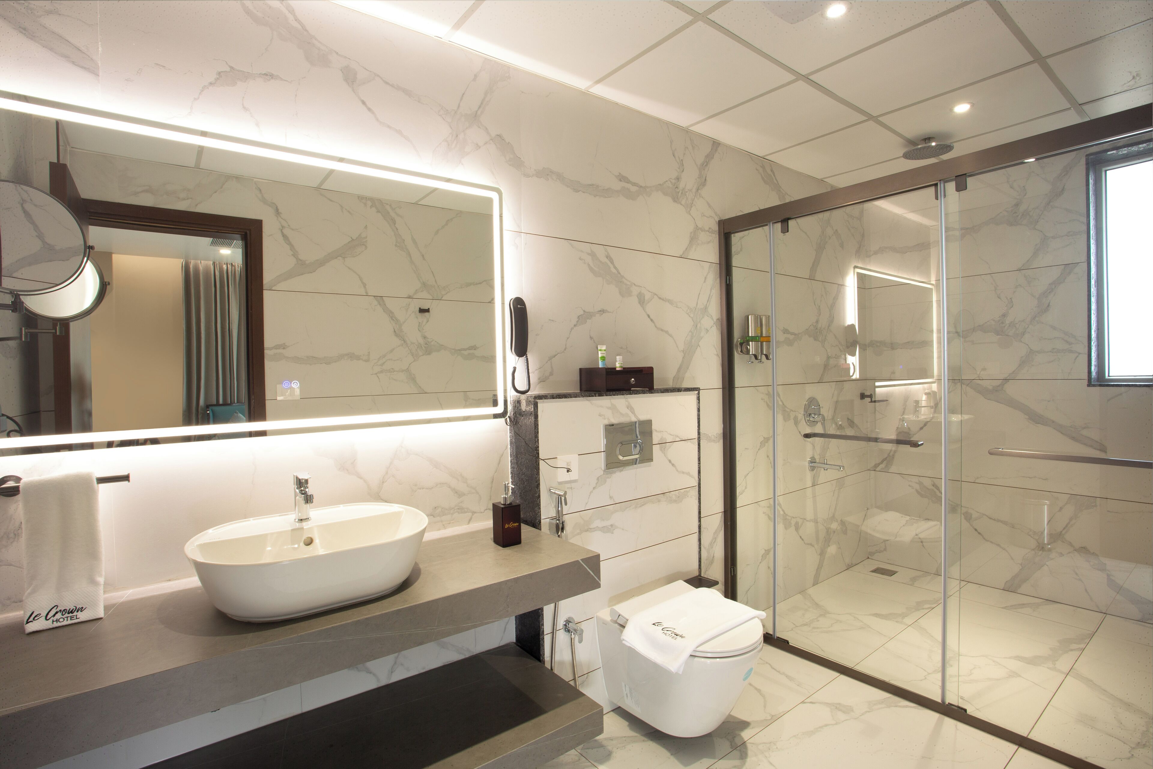 Un baño moderno con un espejo grande, un lavabo, un inodoro y una ducha con mampara de vidrio.