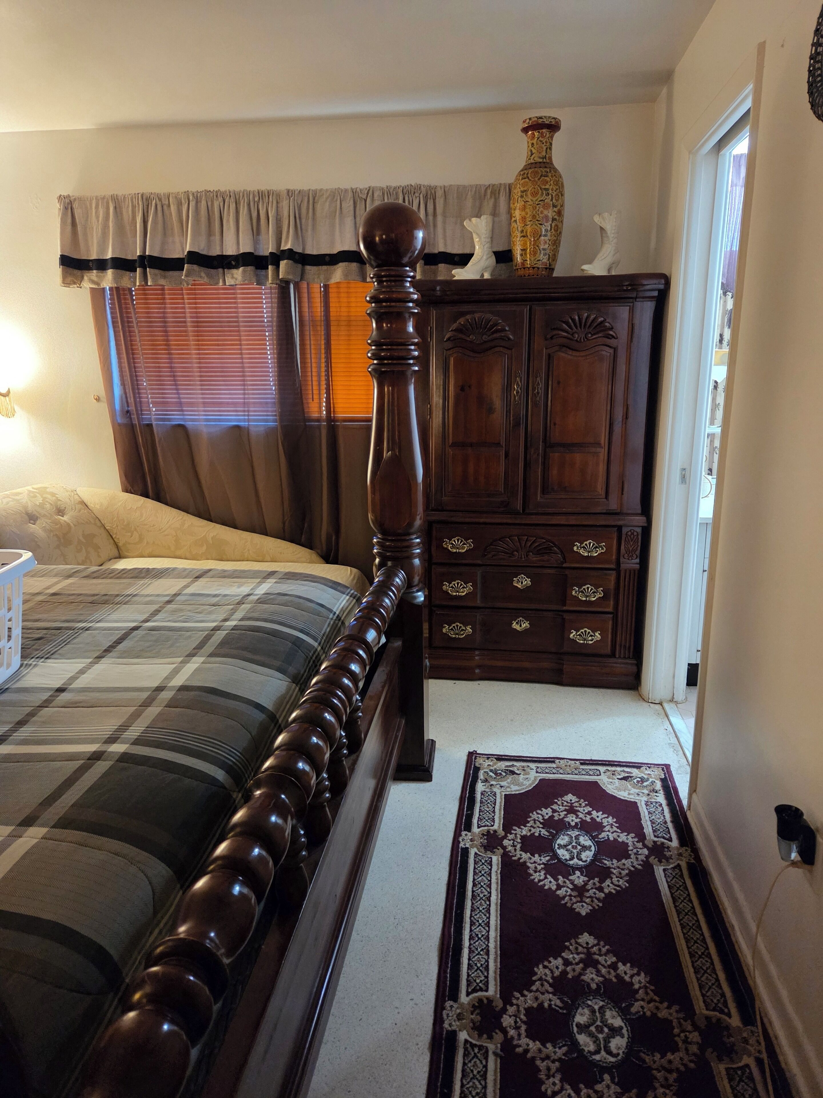 A bedroom with a bed, a dresser, a rug, and a window with curtains.