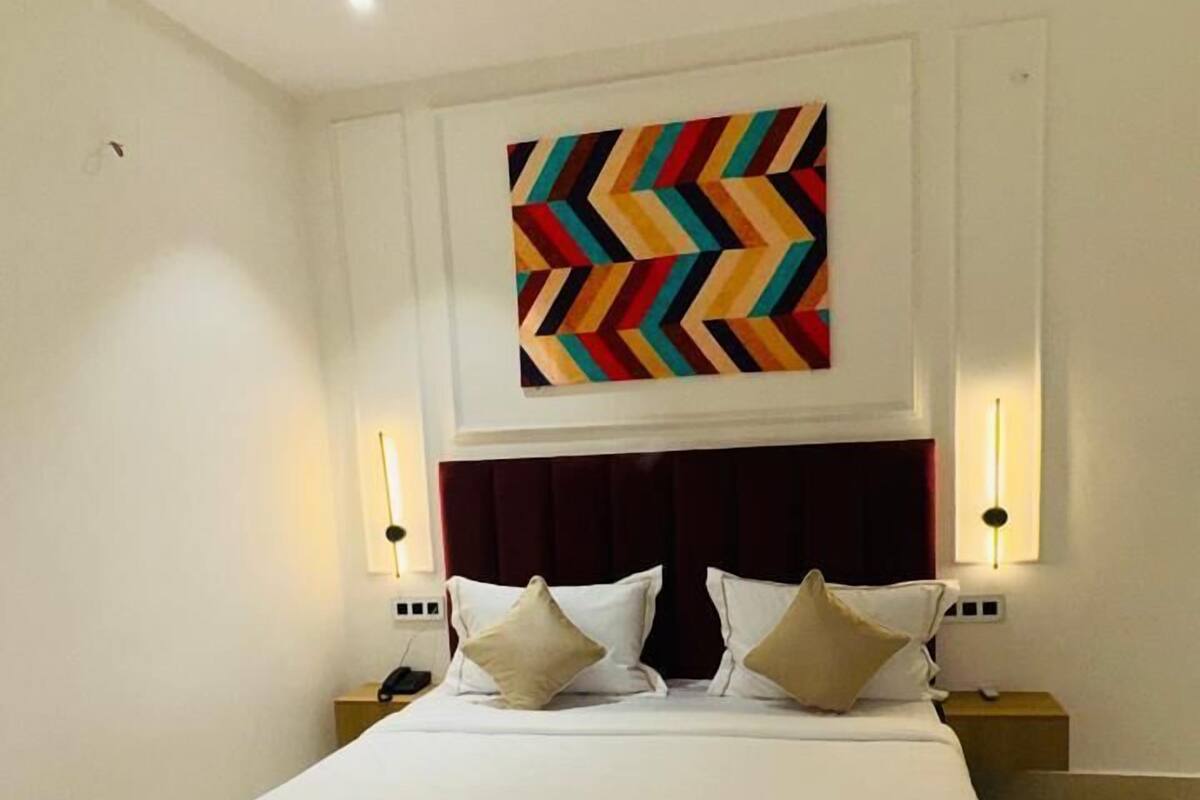 A modern hotel room with a large bed, a ceiling fan, and a colorful abstract painting on the wall.