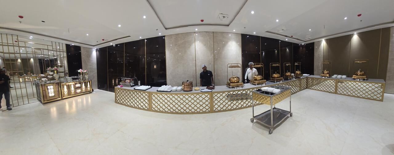 A modern hotel lobby with a curved reception desk, a seating area, and a large window offering a view of the cityscape.