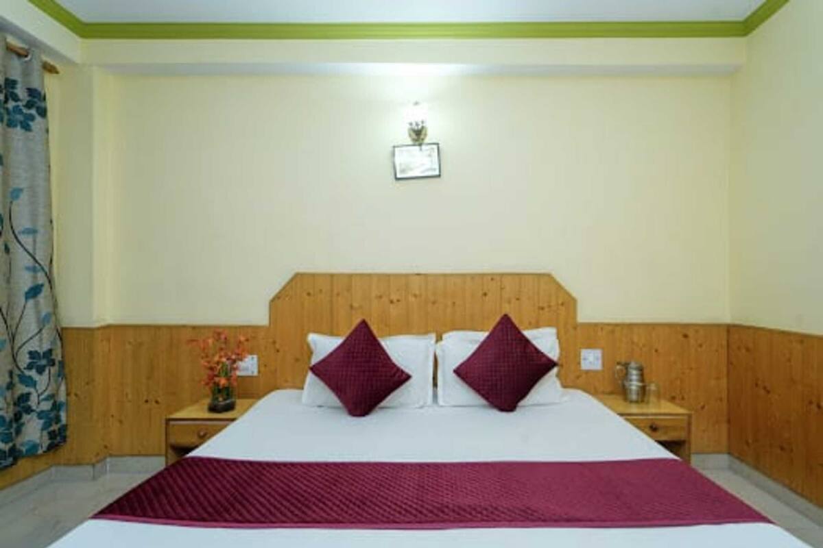Ein Hotelzimmer mit Holz-Kopfteil, einem großen Bett mit zwei Kissen, einem Nachttisch mit Lampe und einem Wandbild.
