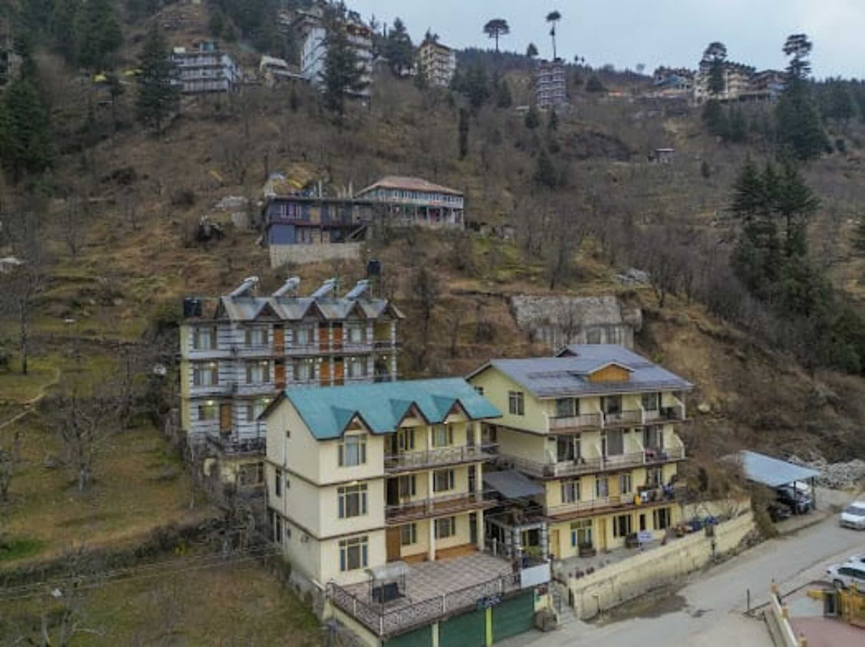 A multi-story building with balconies, located on a hillside with other buildings in the background.