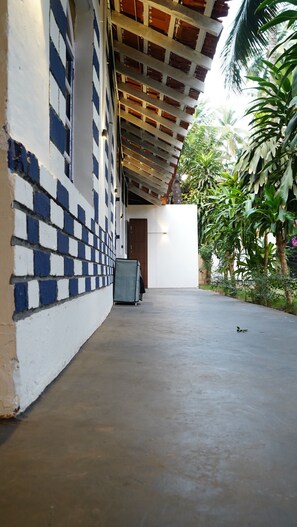A covered outdoor area with a tiled wall, a concrete floor, and a door leading inside. - Garden Aroma Palolem Beach (Canacona)