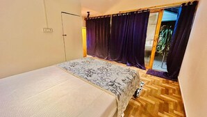 Een slaapkamer met een bed, een raam met gordijnen, een houten vloer en een deur.