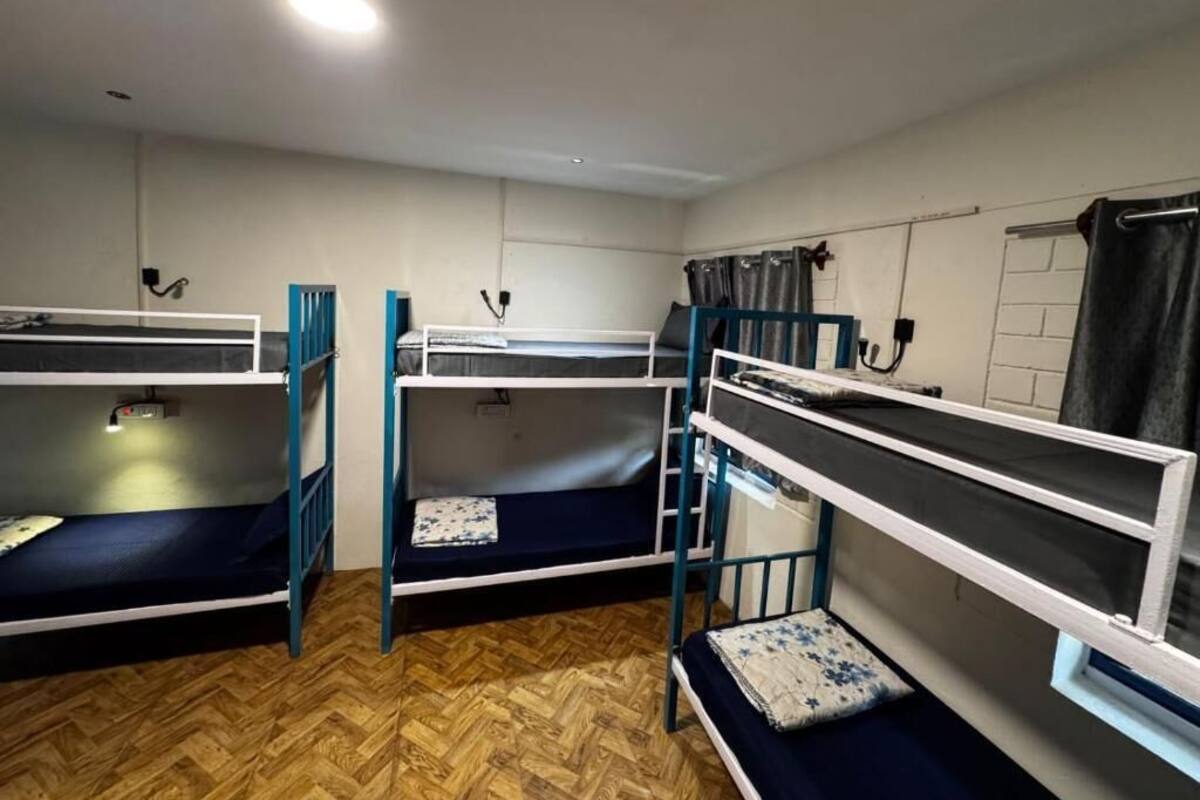 A dormitory room with bunk beds, a wooden floor, and a window with curtains.