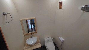 Un baño pequeño y funcional con tocador de madera, lavamanos, inodoro y ducha.