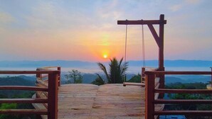 Una terraza de madera con vista al atardecer sobre un paisaje montañoso.