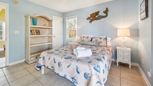 Un dormitorio con cama, mesita de noche, estantería y ventilador de techo.