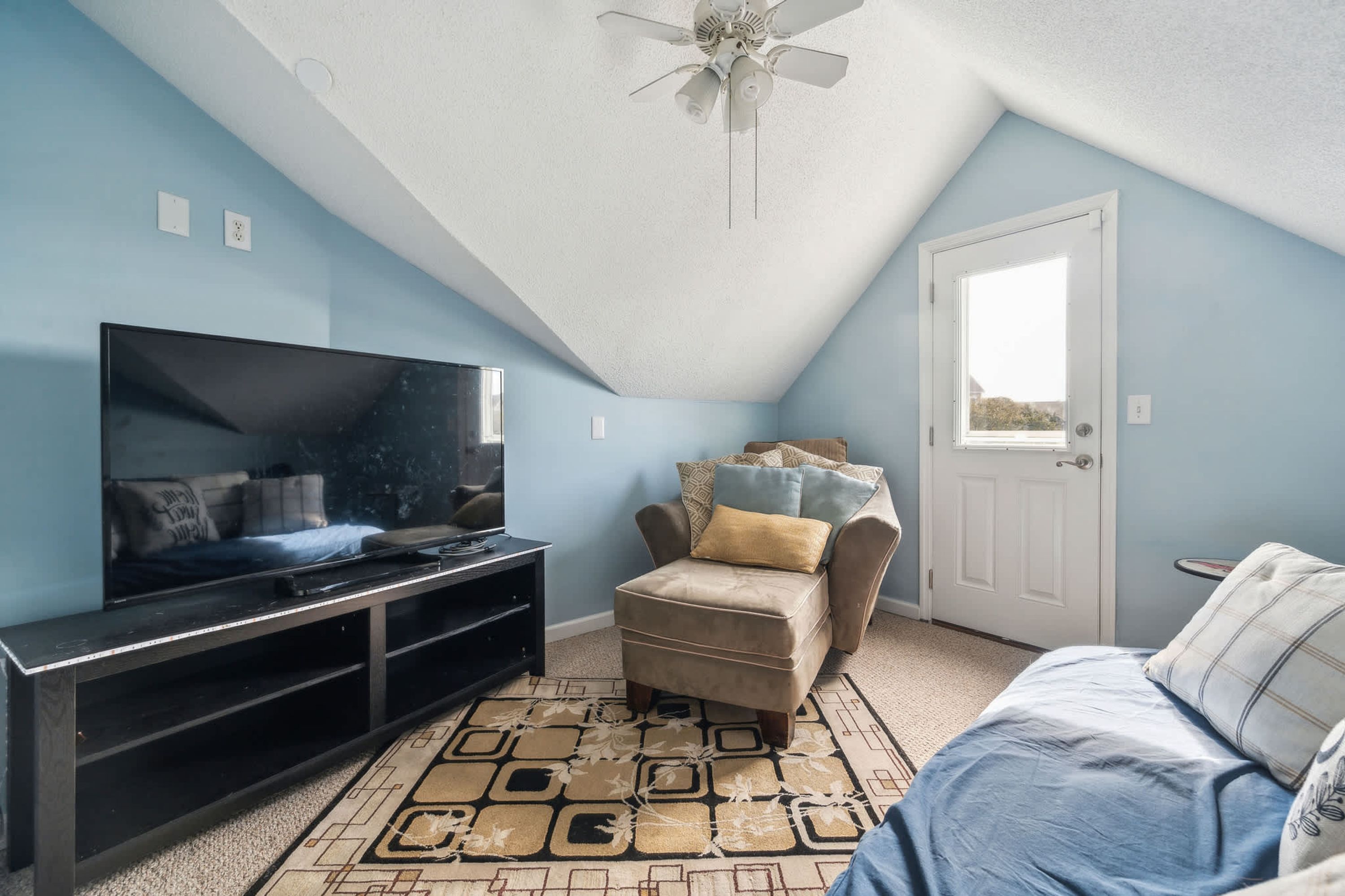 A room with a television on a stand, a sofa, a patterned rug, and a ceiling fan.