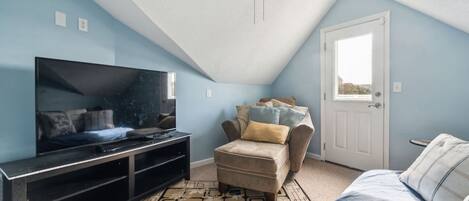A room with a television on a stand, a sofa, a patterned rug, and a ceiling fan.