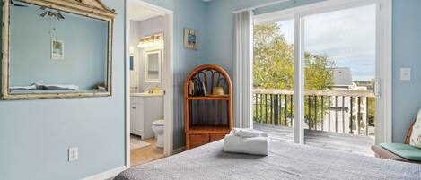 Een slaapkamer met een groot bed, een houten stoel, een spiegel en uitzicht op het balkon.