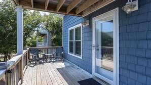 Una terraza techada con mobiliario exterior, una puerta corrediza de vidrio y vista a una casa vecina.