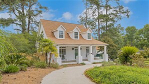 A two-story house with a covered porch, surrounded by lush greenery and trees. - Augusta Getaway Near Masters Porch Swing Deck (Augusta)