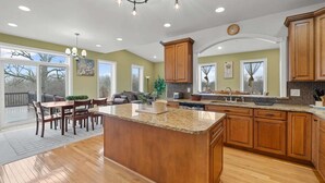 A spacious kitchen with a large island, wooden cabinets, and a dining area with a table and chairs. - Luxury Ann Arbor Stay Theater Gym Game Room Spa (Ann Arbor)