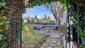 Un mur de pierre avec un portail en métal, un chemin de pierre et du mobilier d’extérieur, le tout dans un cadre résidentiel.