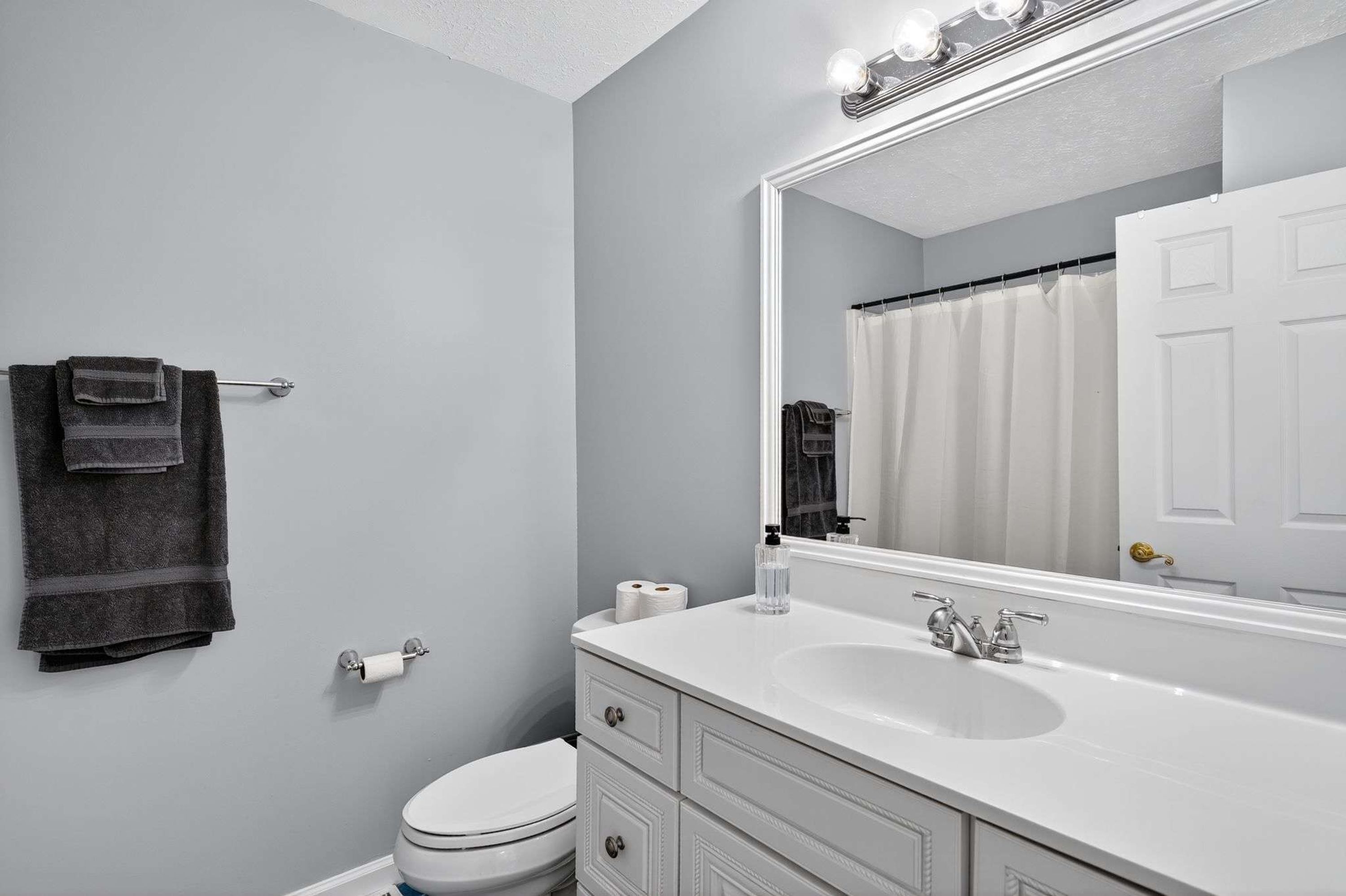 A bathroom with a white sink, a large mirror, a towel rack with a towel, a toilet, and a shower curtain.