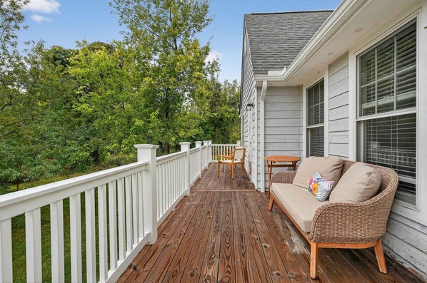 A wooden deck with a white railing, a wicker sofa, and a small table. - Waterfront Kent Island Retreat 5BR Sleeps 12 Near Weddings Annapolis (Stevensville)