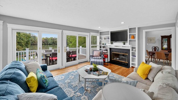 A spacious living room with a large sliding glass door leading to a deck, a fireplace, and a dining area with a view of greenery. - Waterfront Kent Island Retreat 5BR Sleeps 12 Near Weddings Annapolis (Stevensville)