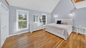 A bedroom with a sloped ceiling, a bed with a white headboard, a dresser, a nightstand, and a window with blinds. - Waterfront Kent Island Retreat 5BR Sleeps 12 Near Weddings Annapolis (Stevensville)