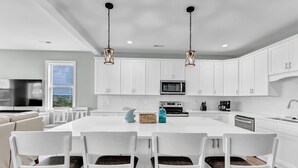 A modern kitchen with white cabinetry, a central island with chairs, a microwave, and a coffee maker. - Walk to Beach Pool Ocean View Parking Bunk Beds (Holly Ridge)
