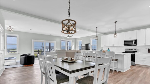A spacious kitchen with white cabinetry, a central island, and a dining area with white chairs and a table. - Walk to Beach Pool Ocean View Parking Bunk Beds (Holly Ridge)