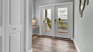 A hallway with a wooden floor, a white door, and a view of a balcony with a railing. - Walk to Beach Pool Ocean View Parking Bunk Beds (Holly Ridge)