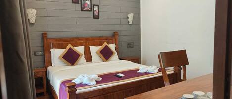 A neatly arranged hotel room with a wooden bed, a small table with a pitcher and glasses, and a chair.