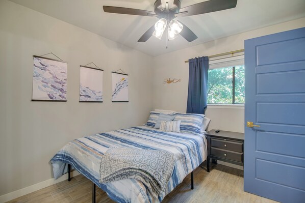 Une chambre à coucher comprenant un lit, une table de chevet, une commode, un ventilateur de plafond et des œuvres d’art murales.