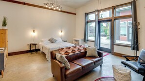 A modern hotel room with a brown leather sofa, a bed with a patterned throw, a small side table, and a large window with curtains. - 3 Blocks to Dtwn! Cozy Sedro-Woolley Retreat! (Sedro-Woolley)