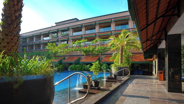A hotel with a pool area, outdoor seating, and a large planter with greenery.